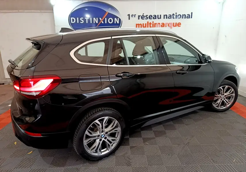 BMW X1 sDrive16d noire vue de profil droit, avec feux arrière allumés dans un showroom intérieur.