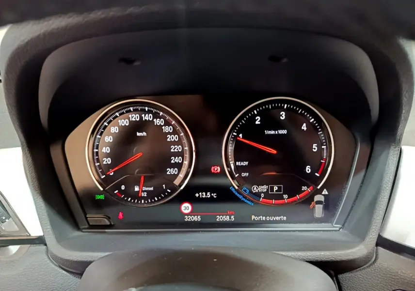 Vue rapprochée du tableau de bord numérique du BMW X1 noir, affichant la vitesse, le régime moteur et les alertes.