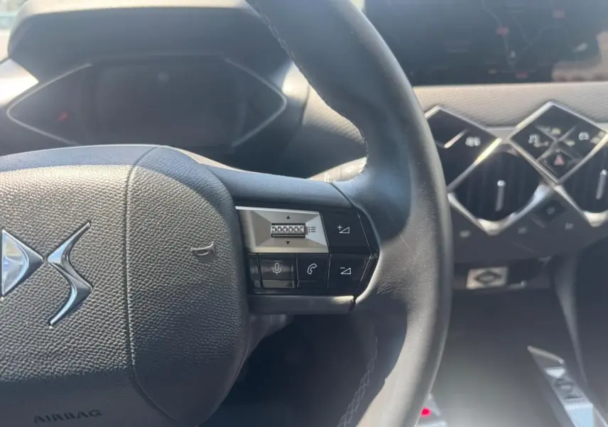Vue rapprochée du volant noir et de la console centrale avec commandes en losange du DS3 100 BVM6 Bastille gris 2024.