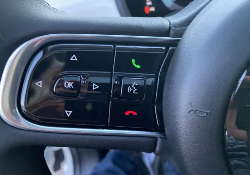 Gros plan sur les commandes noires du volant du Fiat 500 électrique blanc, avec boutons appel et navigation intégrés.