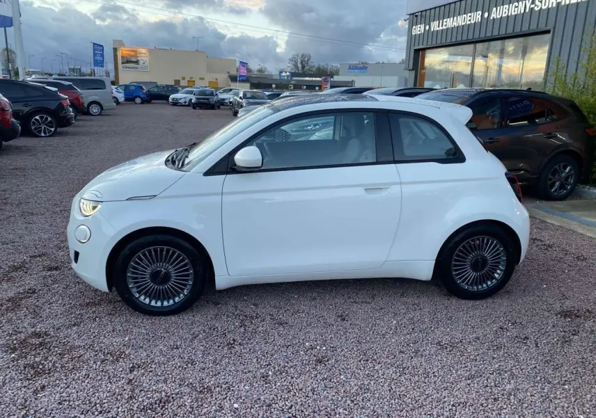 Profil côté gauche d'une FIAT 500 électrique blanche 2022 avec jantes alliage 16'' Icône sur parking extérieur.