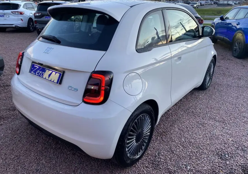 Vue 3/4 arrière droite d'une FIAT 500 électrique blanche avec jantes alliage 16'' Icône sur parking.