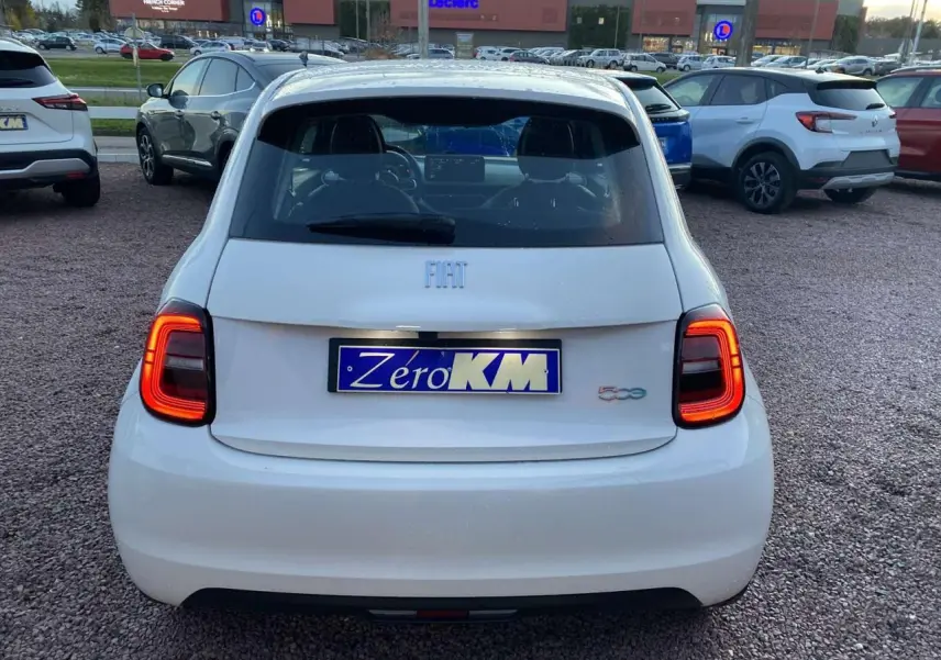 Vue arrière d'une FIAT 500 électrique blanche 2022 avec feux arrière allumés sur parking extérieur.
