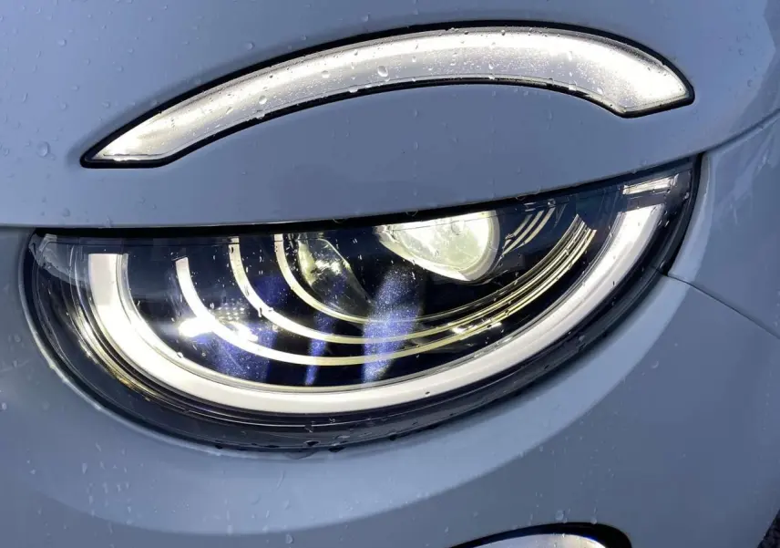 Gros plan sur le phare avant droit blanc d'une FIAT 500 électrique 118CV Icône avec gouttes d'eau visibles.