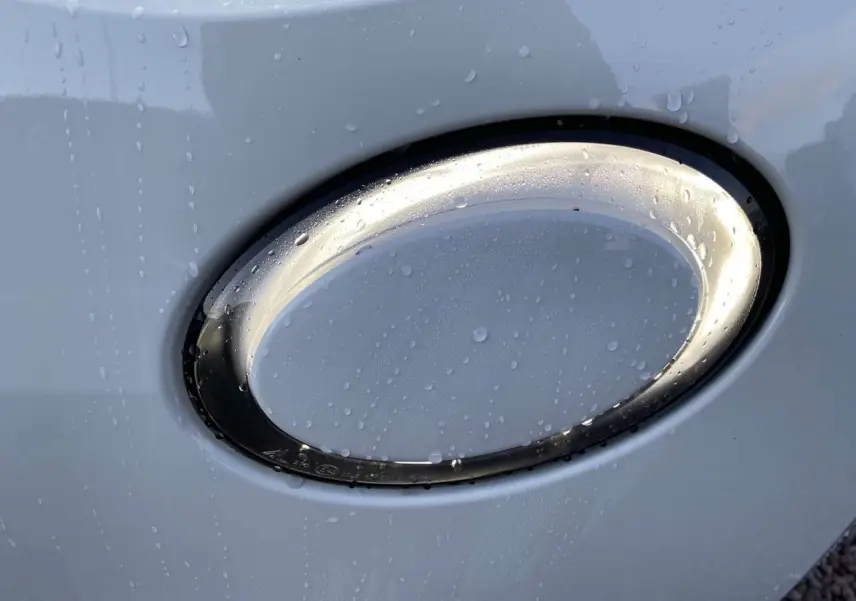 Gros plan sur le feu avant oval blanc d'une Fiat 500 électrique 2022 avec gouttes d'eau sur la carrosserie.