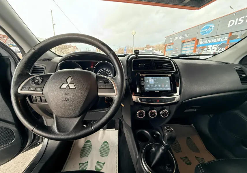 Vue intérieure avant centrée sur le volant noir et la console centrale avec écran tactile du Mitsubishi ASX gris de 2015.