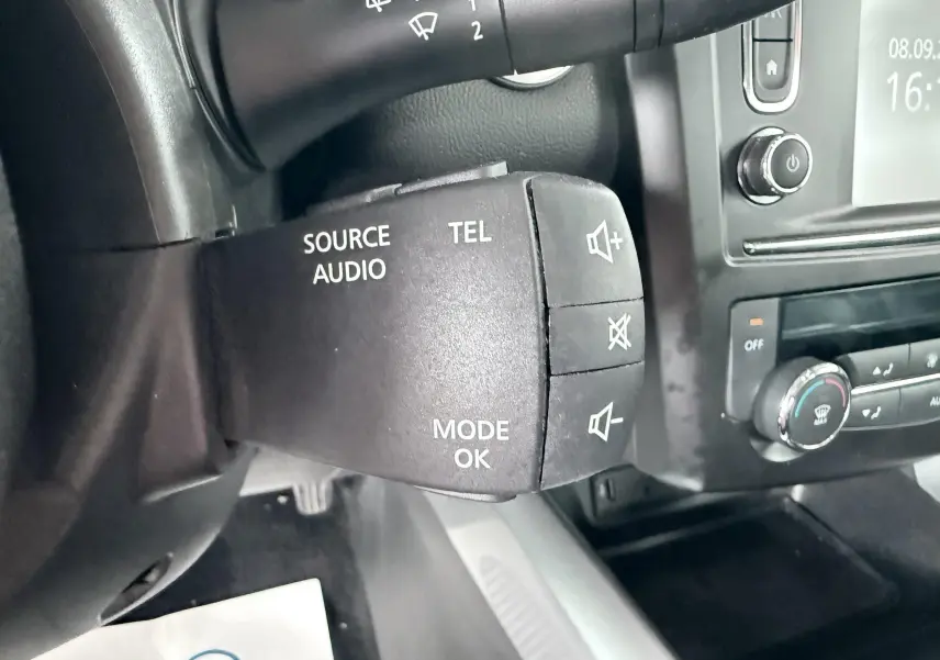 Gros plan sur la commande audio au volant noir dans l'habitacle du Renault Kadjar gris, avec tableau de bord et commandes clim visibles.