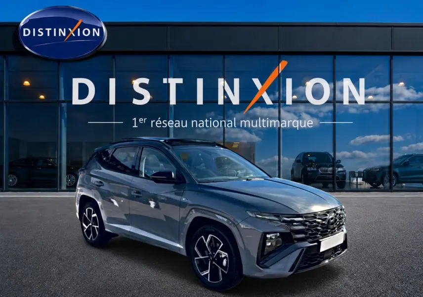 Hyundai Tucson gris shadow en 3/4 avant droit, avec calandre noire et jantes alu distinctives devant showroom Distinxion.