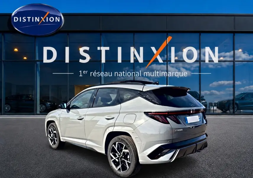 Vue 3/4 arrière droite du Hyundai Tucson gris shadow avec jantes alu et toit noir devant une vitrine Distinxion.