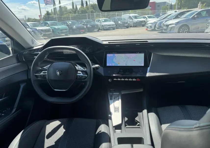 Intérieur noir de la Peugeot 308 Hybrid 2024 vu de face, avec volant compact et écran tactile central affichant une carte.