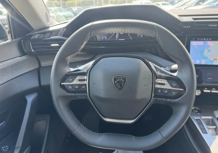 Vue centrée sur le volant noir du Peugeot 308 Hybrid 2024, avec tableau de bord numérique et écran tactile visible.