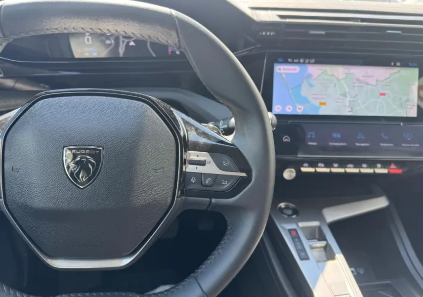 Vue intérieure centrée sur le volant Peugeot noir et le cockpit numérique avec écran tactile affichant une carte.