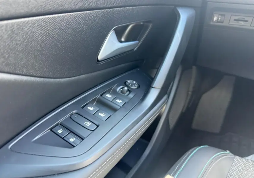 Gros plan sur la porte côté conducteur de la Peugeot 308 Hybrid noire, montrant les commandes des vitres et la poignée intérieure.