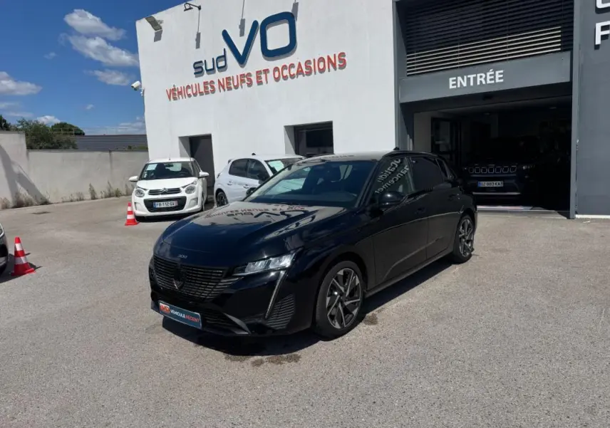 PEUGEOT 308 Hybrid noir vue 3/4 avant droit, jantes alliage 17 pouces, stationnée devant un garage Sud VO.