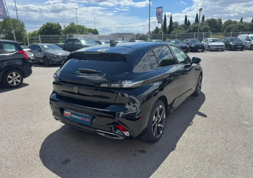 Vue 3/4 arrière droite d'une Peugeot 308 Hybrid 136 noire avec jantes alliage 17 pouces, stationnée en extérieur.