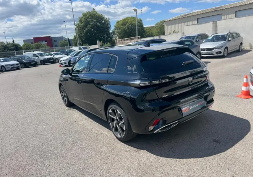 Vue 3/4 arrière droite d'une Peugeot 308 Hybrid noire 2024 avec jantes alliage 17 pouces, feux LED et toit noir brillant.