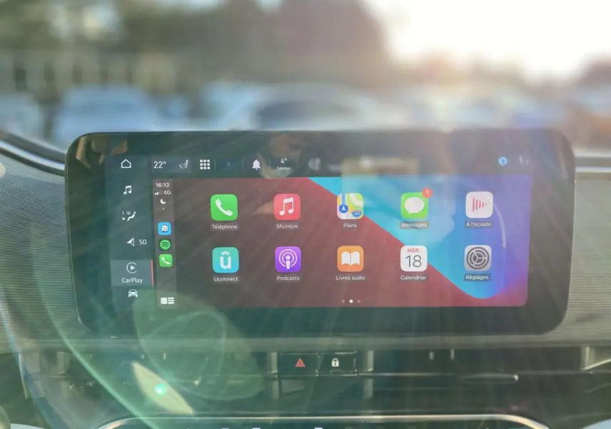 Écran tactile central de la FIAT 500 électrique 2022 affichant Apple CarPlay avec reflets lumineux à l'avant.