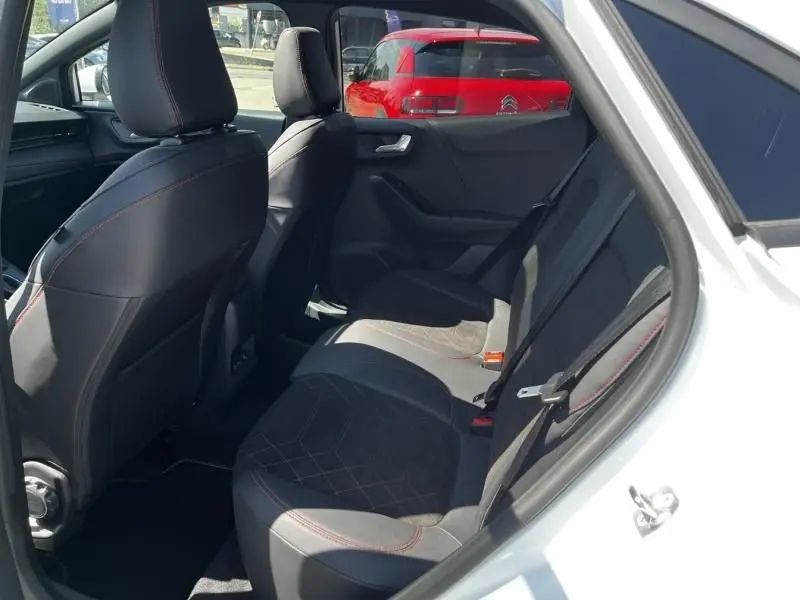 Vue intérieure arrière côté droit du Ford Puma blanc 2025, sièges en tissu noir avec surpiqûres rouges visibles.