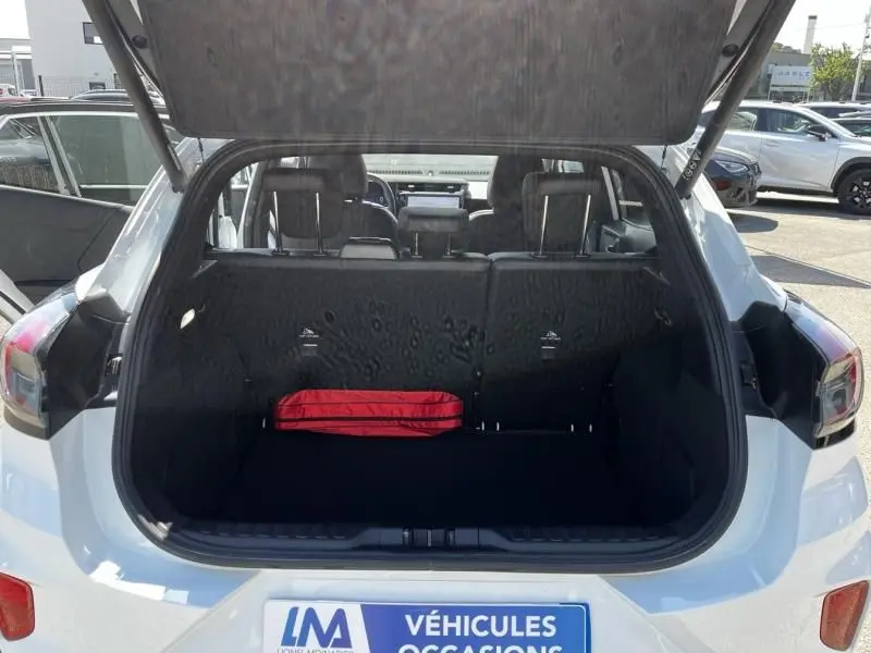 Vue arrière du coffre ouvert du Ford Puma blanc 2025, avec un kit de sécurité rouge visible à l'intérieur.