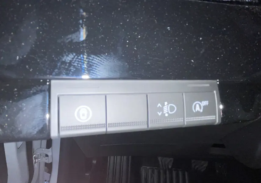 Gros plan sur les commandes de réglage des phares et désactivation du start-stop dans l’habitacle noir d’une Renault Clio VI gris Rafale.