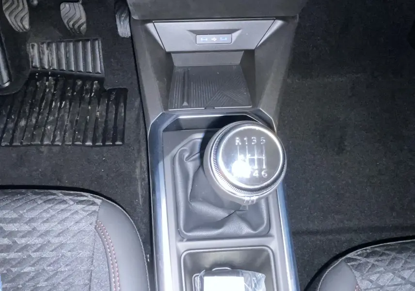 Vue plongeante sur la boîte manuelle et le levier de vitesse de la Renault Clio gris Rafale, avec pédales et sièges partiellement visibles.