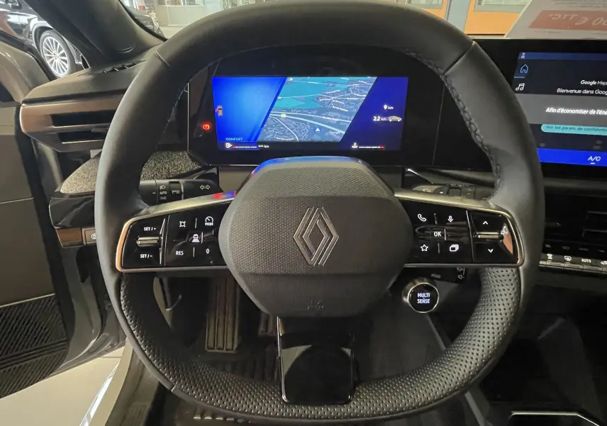 Vue centrée du volant noir perforé de la Renault Clio VI TCe 115ch Techno avec écran numérique et commandes intégrées.