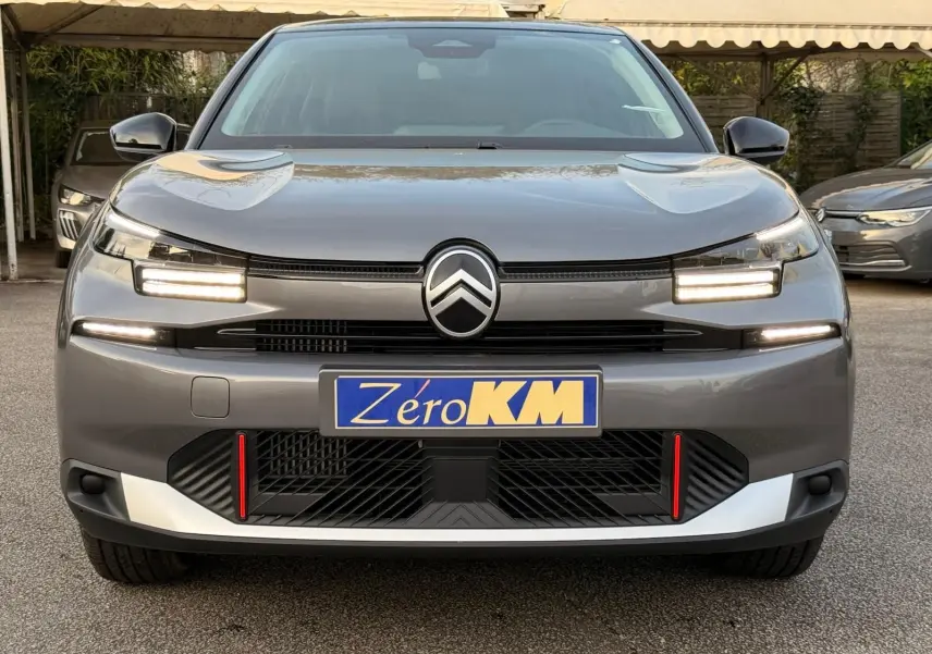Vue de face d'une Citroën C4 hybride gris Mercury avec phares LED allumés et détails rouges sur la calandre.