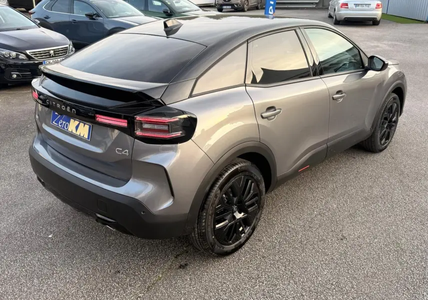 Vue 3/4 arrière droite d'une Citroën C4 hybride 2025 gris Mercury avec toit noir et jantes noires distinctives.