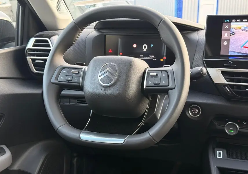 Vue intérieure centrée sur le volant cuir noir du Citroën C4 hybride 2025 avec tableau de bord numérique et écran tactile.