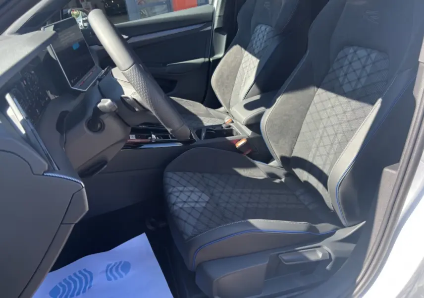 Vue intérieure côté conducteur de la Volkswagen Golf TDI 150 R-Line avec sièges en tissu noir et surpiqûres bleues.