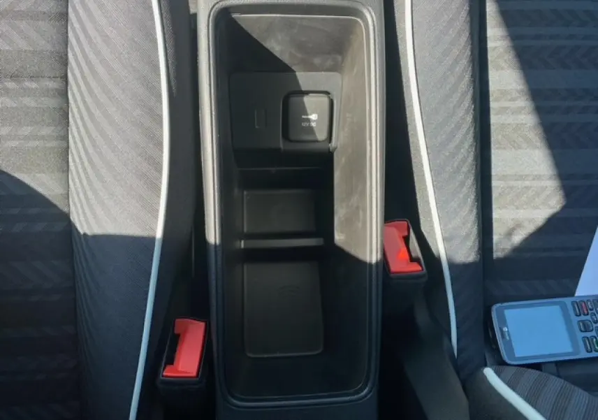 Vue plongeante sur la console centrale noire de la Fiat 500 électrique blanche avec sièges gris et ceintures rouges.