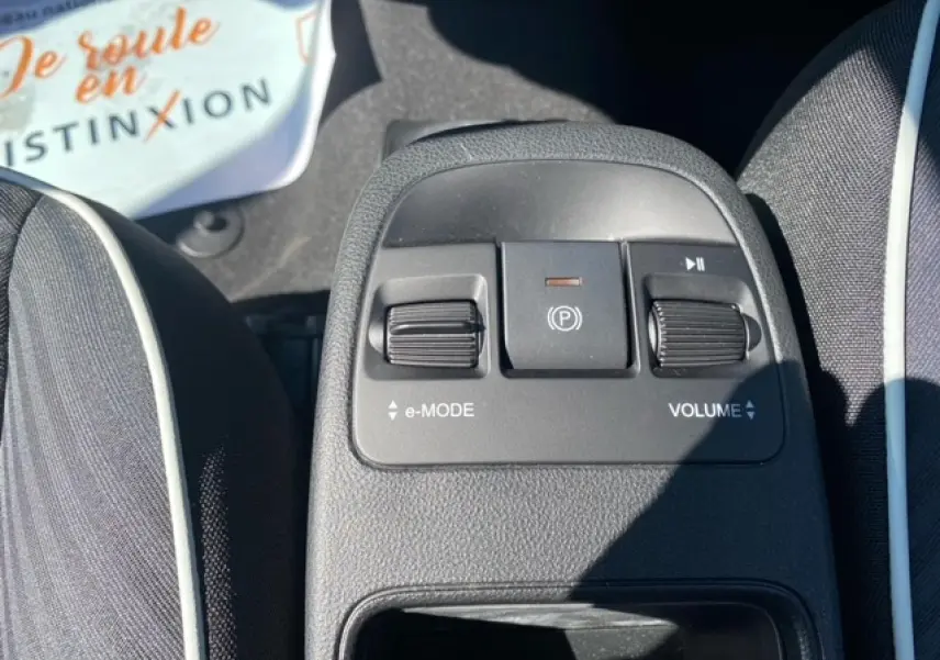 Gros plan sur la console centrale entre les sièges noirs de la Fiat 500 électrique blanche, avec commandes e-mode et volume.