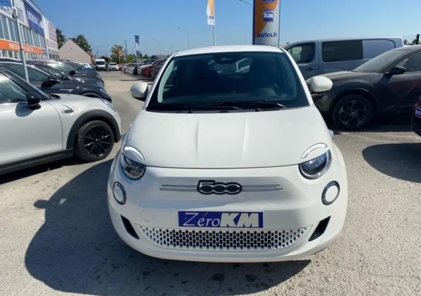 Vue frontale d'une FIAT 500 électrique blanche Ice White avec logo 500 et plaque Zéro KM visible.