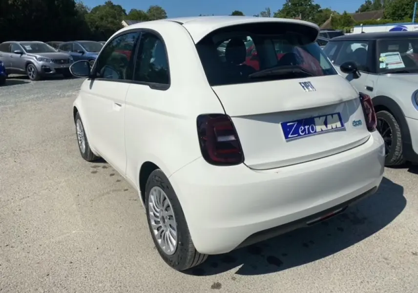 Vue 3/4 arrière droite d'une FIAT 500 électrique blanche Ice White avec feux arrière foncés sur parking extérieur.
