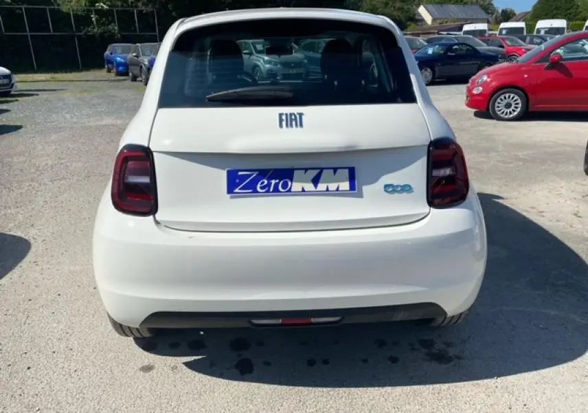 Vue arrière d'une FIAT 500 électrique blanche avec feux arrière foncés et plaque "Zero KM" visible.