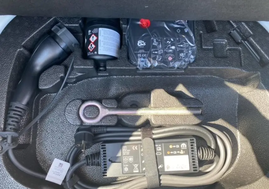Gros plan sur le compartiment de rangement sous coffre d'une FIAT 500 électrique blanche avec câble de recharge et outils.