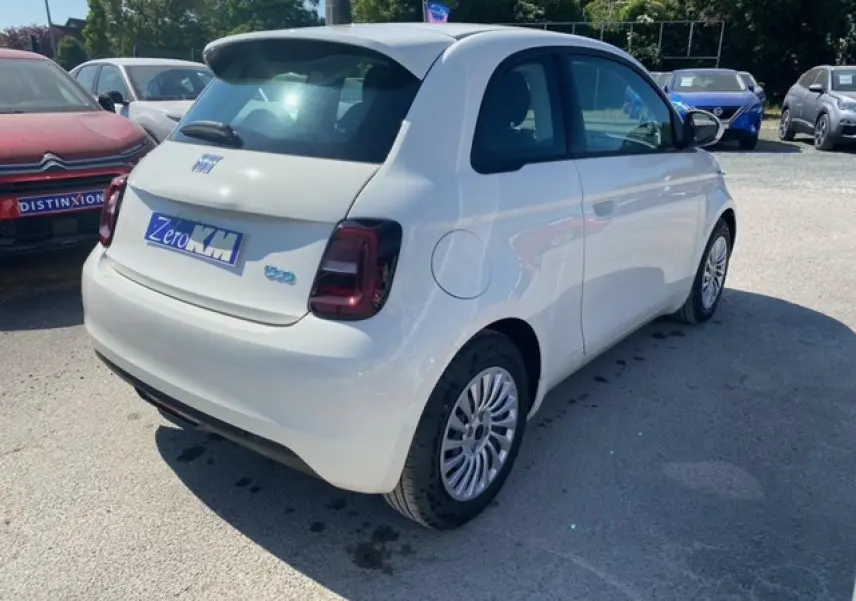 Vue 3/4 arrière droite d'une FIAT 500 électrique blanche Ice White avec feux arrière foncés sur parking extérieur.