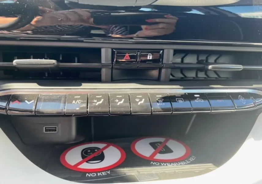 Gros plan sur la console centrale noire de la Fiat 500 électrique blanche, montrant les commandes de climatisation et ventilation.