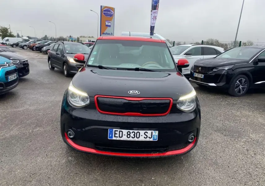 Vue avant d'une KIA Soul électrique noire avec toit et détails rouges, feux allumés sur parking extérieur.