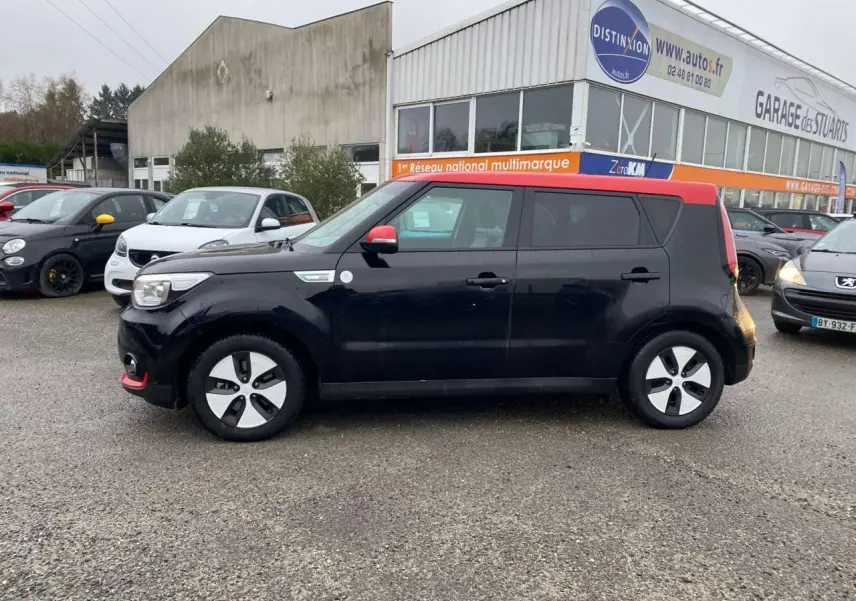 KIA SOUL électrique noir avec toit rouge vu de profil côté gauche sur un parking devant un garage multimarque.