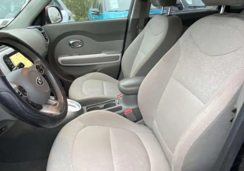 Intérieur avant du Kia Soul électrique 2016, sièges gris clairs et tableau de bord avec écran tactile visible.