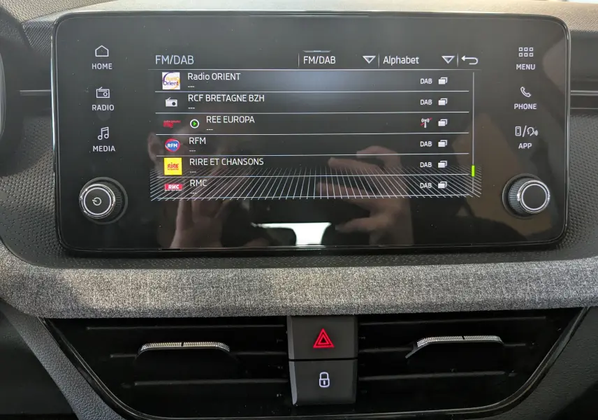 Écran tactile central du Skoda Kamiq 2025 gris graphite, affichant les stations radio FM/DAB avec commandes autour.
