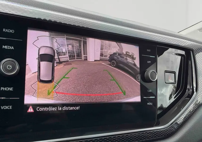 Écran de caméra de recul affichant l’arrière d’une Volkswagen Polo grise en stationnement, vue intérieure console centrale.
