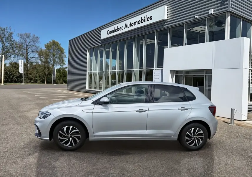 Vue latérale droite d'une Volkswagen Polo grise 2025 garée devant un bâtiment de concession automobile.