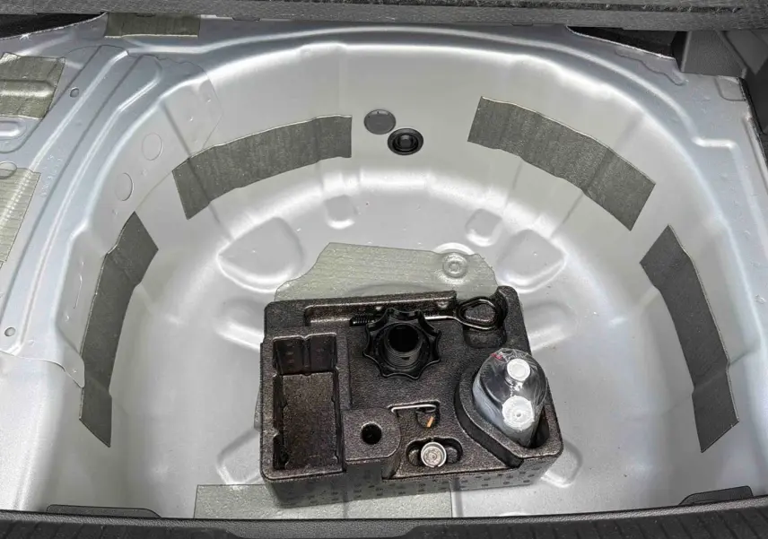 Vue plongeante sur le coffre ouvert d'une Volkswagen Polo grise, montrant le rangement pour roue de secours et outils.