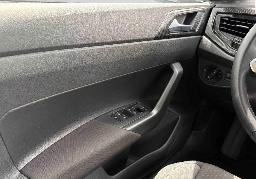 Vue intérieure côté conducteur de la Volkswagen Polo 2025, montrant la portière avec commandes électriques et accoudoir gris foncé.