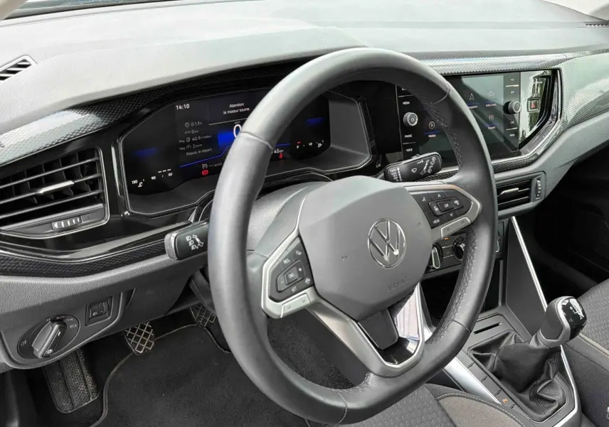 Vue intérieure côté conducteur du tableau de bord gris et volant multifonctions d'une Volkswagen Polo 2025 avec boîte manuelle.