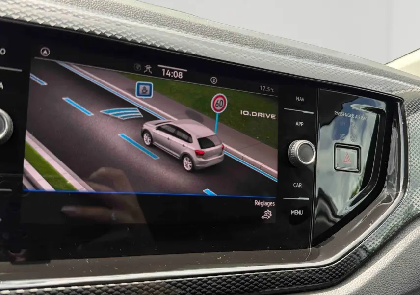 Écran tactile intérieur affichant la caméra de recul d'une Volkswagen Polo grise vue en 3/4 arrière sur route.