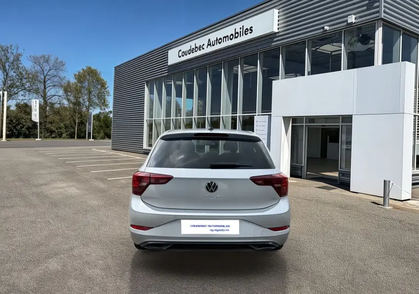 Vue arrière d'une Volkswagen Polo grise 2025 garée devant un bâtiment moderne de concession automobile.