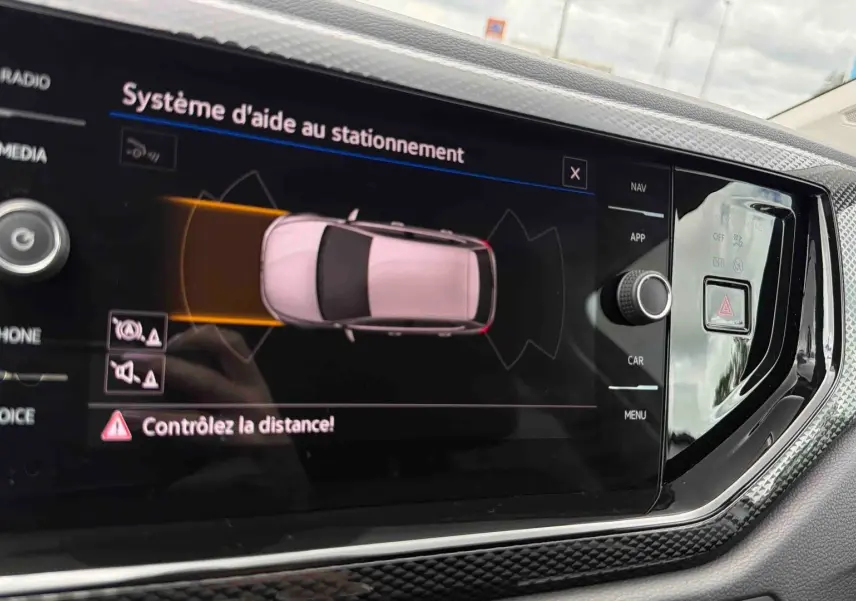 Écran tactile central du Volkswagen Polo 2025 montrant l'aide au stationnement avec vue aérienne du véhicule gris.